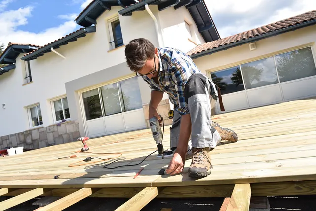 Carpenter framing a new wooden deck behind a home