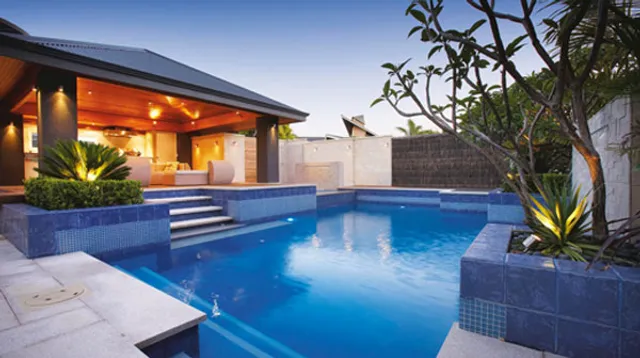 Modern pool and light stone deck with outdoor living area at dusk